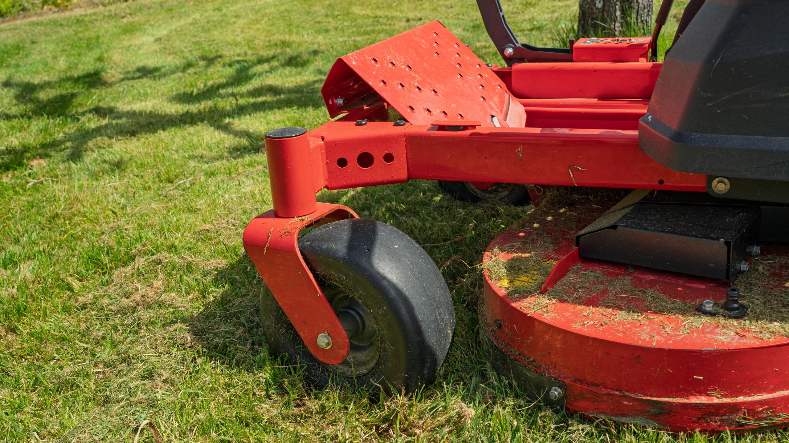 Close-up of a riding lawn mower deck and wheels on grass